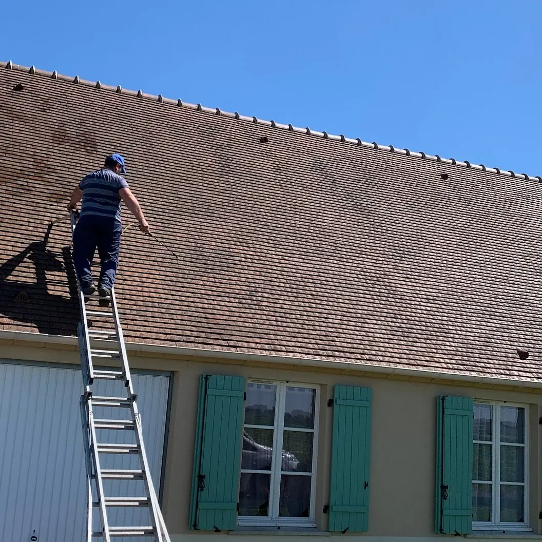 Artisan de l'entreprise sur son échelle, en intervention sur une toiture en tuiles